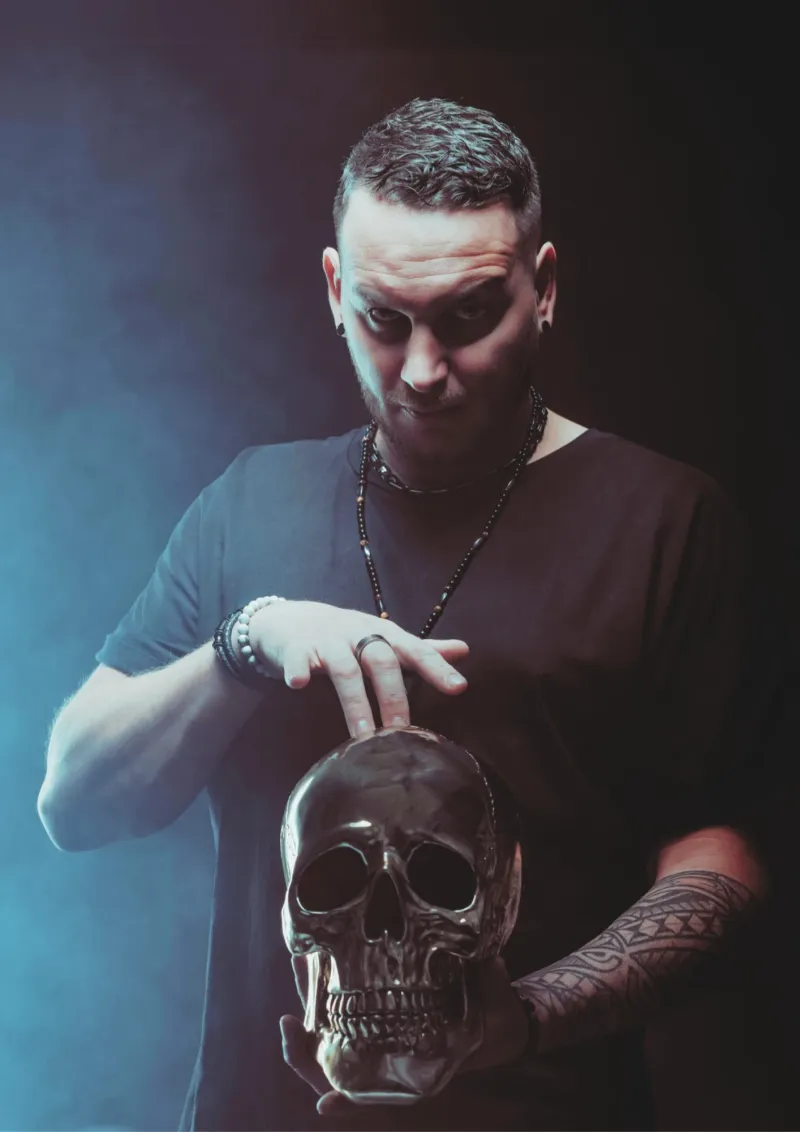 R'Key, hypnotiseur de spectacle, la main posée sur un crâne argenté, dans une lumière bleutée